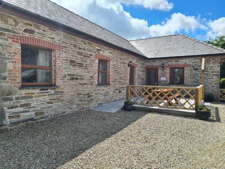 A stone building with wooden windows and a small fenced patio with a table and chairs at Swallow Cottage in Llanboidy