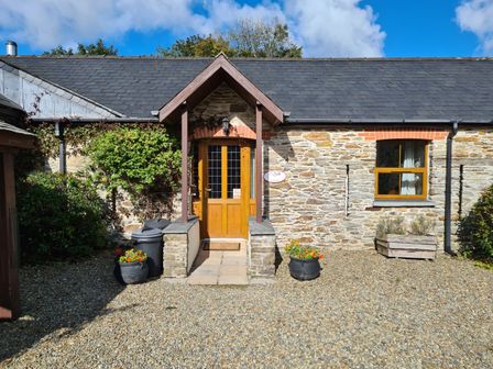 Stone cottage exterior with wooden door and window a gravel ground and flower pots at Sandpiper Cottage in Llanboidy