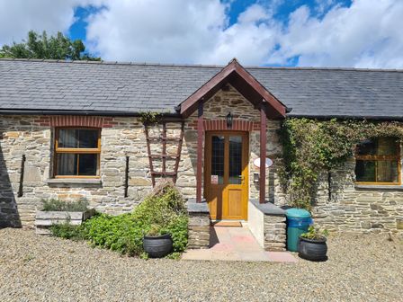 A stone cottage with wooden door and windows a small porch and plants at Puffin Cottage in Llanboidy