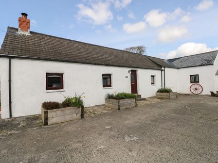 A white building with a brown door and three windows with planters in front at Hill Top Farm Cottage Martletwy near Narbeth