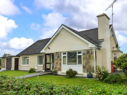 A house with a sloped roof chimney and garage surrounded by a lawn and shrubs at Eileen's in Aughavas near Mohill County Leitrim