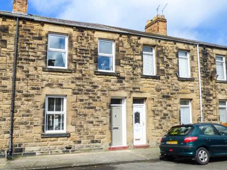 A row of stone terraced houses with doors and windows and a car parked on the street at Silversands Cottage in Amble-by-the-Sea