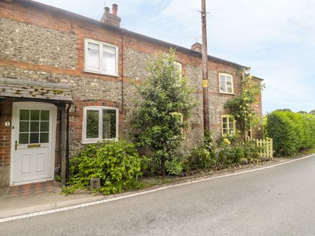 A street view of a cottage with brick and stone walls with bushes and flowers outside at Apple Tree Cottage in Shillingstone near Sturminster Newton