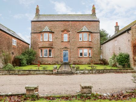 A stone house with a blue front door two side buildings and a gravel driveway at Eden House Edenhall near Penrith