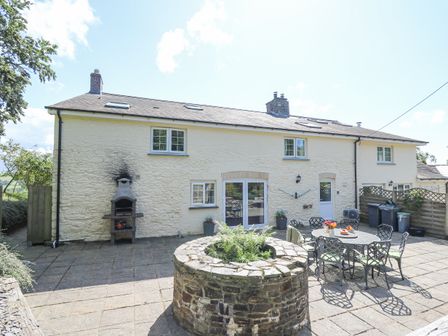 A stone patio area with a round brick planter and outdoor dining table set outside a stone house at Penuwch Fach in Aberystwyth