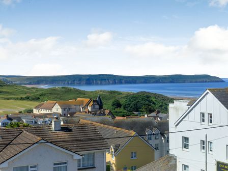A coastal town with houses, green hills, a hotel, and a sea cliff in the background at Glenwood in Woolacombe
