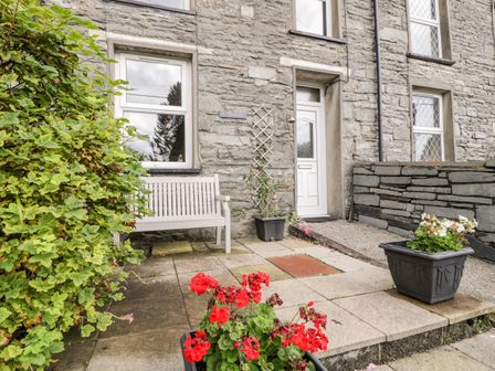 A stone house exterior with a white bench near a window and two flower pots on the pavement at Ty Gwynn in Tanygrisiau
