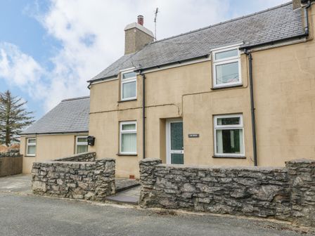 A beige house with multiple windows and a stone wall in front at Tir Bedw in Edern near Morfa Nefyn