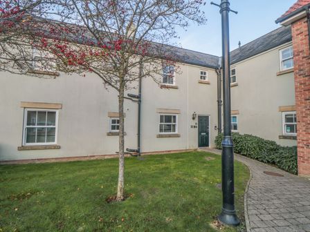 A courtyard with a tree and a lamp post in front of a beige two story building with multiple windows and a green door at Greengables The Bay near Filey