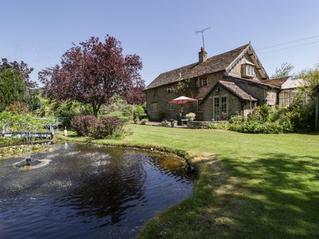 A stone house with a pond and fountain in the garden at Lower Court Byre in Kinsham near Lingen