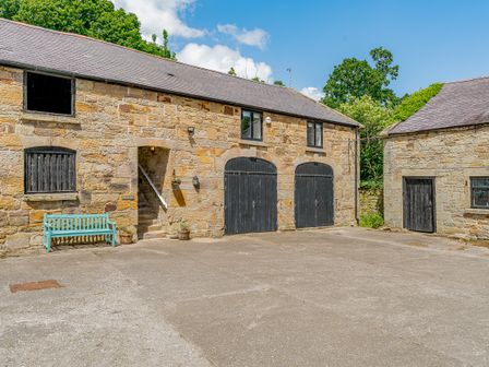 Stone buildings with black doors and a blue bench on a paved courtyard at The Hayloft in Northop near Chester
