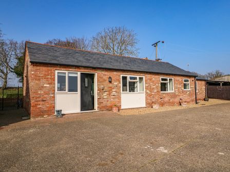 A single story brick house with a black door and multiple windows with potted plants outside at Sunnyside Cottage in Blackborough End near King's Lynn