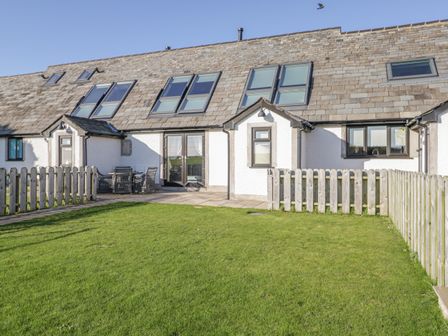 A backyard with a green lawn and a patio with outdoor furniture at Primrose Cottage in Aldingham