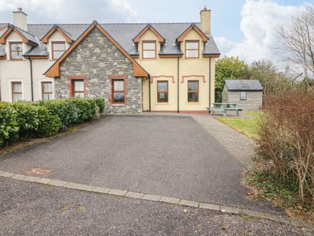 A driveway in front of a stone and stucco house with a picnic table and shed to the side at Kenmare Bay Cottage in Kenmare County Kerry