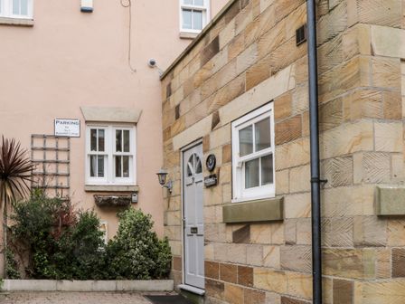The exterior of a stone building with a white door and windows plus greenery and a parking sign at Razorbill Cottage in Whitby