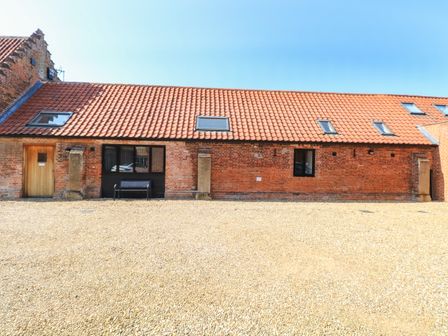 A brick building with a tiled roof and skylights with a gravel foreground at The Long Barn in Morton on the Hill near Lenwade