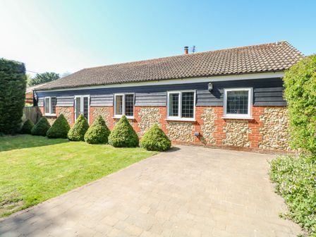 A single-story house with stone and brick walls and a tiled roof with bushes and a paved driveway at The Meadows Cottage in Billingford near Bawdeswell