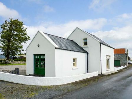 A white cottage with green doors and windows next to a road with a tree nearby at Annies Cottage in Doonamona near Belcarra County Mayo