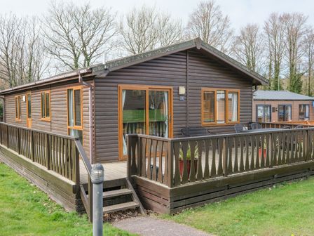 A wooden cabin with a fenced deck and outdoor seating surrounded by grass and trees at High Tide in Rock