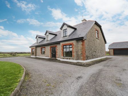 A stone house with three dormer windows and a detached garage on a gravel driveway at Cloonacastle Cottage in Ballinrobe County Mayo