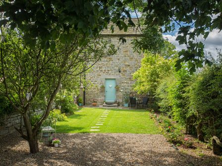 A garden with a stone path and patio furniture in front of a stone building with a blue door at West Wing Cottage in Hexham