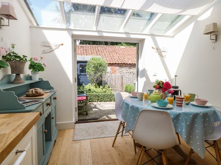 A dining area with a round table covered by a blue polka dot tablecloth and chairs under a glass roof at Bridge Cottage in Aylsham