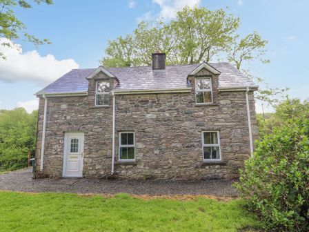 A stone cottage with a white door and four windows surrounded by greenery at Gortagown Cottage in Sneem County Kerry