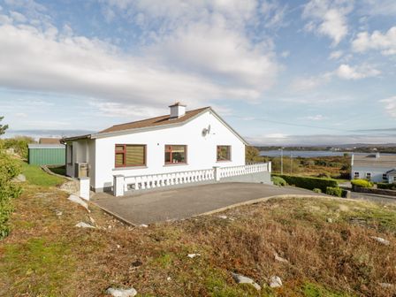 A white single-story house with three windows and a satellite dish on a hill overlooking a body of water at Aras Iosgan in Carraroe County Galway