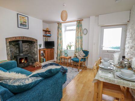 A living room with a fireplace a blue sofa a wooden dining table set and a window with patterned curtains at Rowan Cottage in Builth Wells