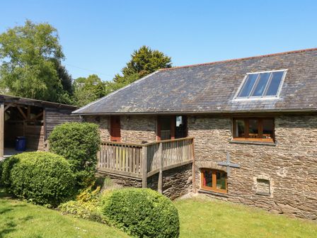 A stone building with a wooden deck and bushes in front at Cowslip Barn in Cornworthy near Dittisham