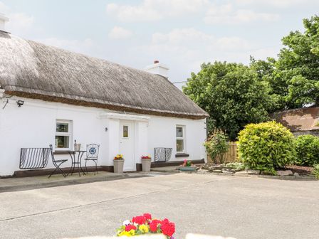 White thatched cottage with outdoor table and chairs near entrance and garden shrubs at Whispering Willows - The Thatch in Carndonagh County Donegal