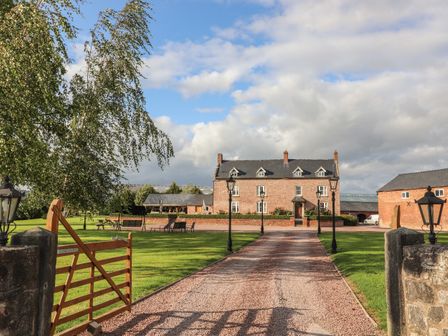 A gravel driveway leading to a brick house with lamp posts and a wooden gate at Rhandregynwen Hall in Four Crosses