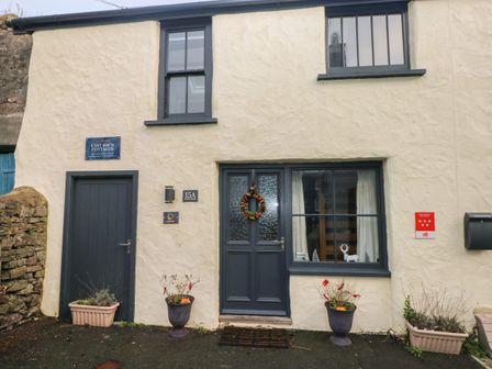 Exterior of a cream-colored cottage with dark blue doors and windows and flower pots outside at Stable Cottage in Pembroke