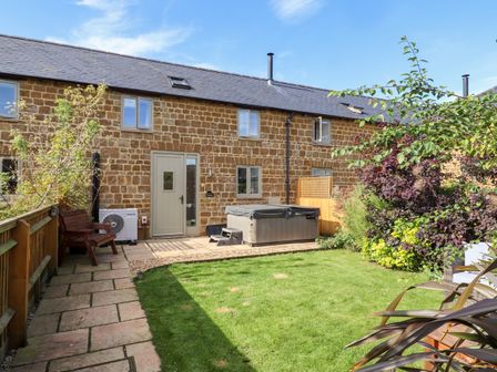 A backyard with stone patio grass lawn bench hot tub and plants at Cow Byre Great Tew near Chipping Norton