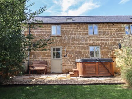 A stone house with a bench and a hot tub in the garden patio at The Stables in Great Tew near Chipping Norton