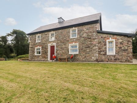 A stone house with a red door and six windows with a lawn in front at Oak Wood House in Kenmare The Ring of Kerry