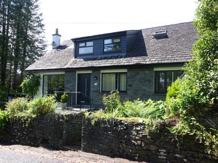 A stone house with a slate roof and garden surrounded by a stone wall at Wysteria Cottage in Windermere