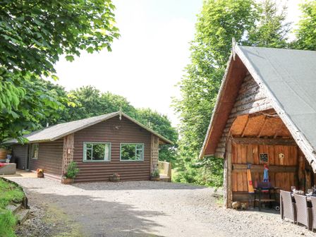 An outdoor area with a wooden cabin and a wooden shelter with chairs and table at Pond Farm Woodlands Ugthorpe