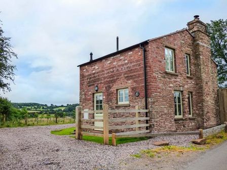 A small stone and brick house with a wooden gate and gravel path in a rural setting at Rose Cottage in Welsh Newton