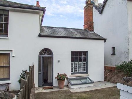 The exterior of a white cottage with a door arched window plants and a brick chimney at Woodland Cottage in Malvern
