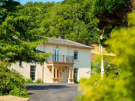 A two story house with a balcony and columns surrounded by trees at Old Rectory House in Caersws