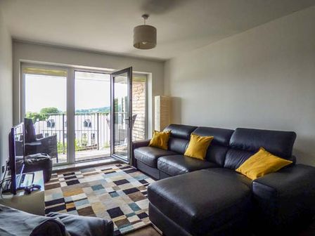 A living room with a black leather sectional sofa with yellow pillows a TV a patterned rug and an open door to a balcony at Tehidy in Charlestown