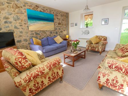 A living room with a stone wall blue sofa floral armchairs coffee table and TV at Seaview in Coverack