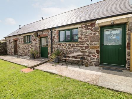 A stone exterior wall with green doors and windows a bench and potted plants on the concrete path at The Long Barn in Hasguard near Little Haven