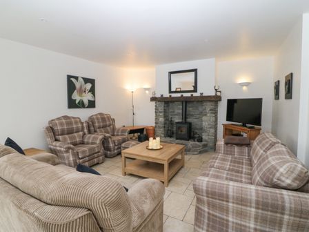 A living room with plaid armchairs sofas a stone fireplace wood stove a wooden coffee table and a television at Rock Lawn Cottage in Kealkill near Bantry County Cork