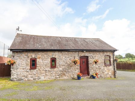 A stone building with three windows and a door surrounded by flower pots and hanging baskets at Bwthyn Ty Newydd in Llangadfan