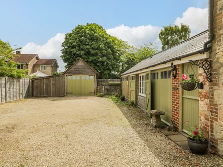 A gravel driveway with green doors on outbuildings and hanging plants at Old Cart Shed in Lyneham near Royal Wootton Bassett