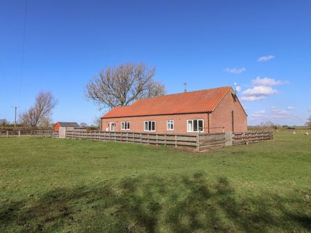 A brick house with a red tile roof surrounded by a wooden fence in a grassy area at Middlegate in Malton