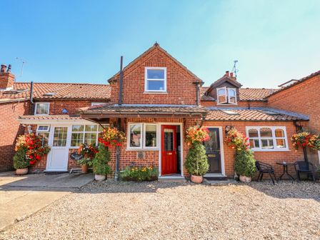 A brick house with a red door and black door with hanging flower baskets and potted plants in front at Camerons Cottage in Swaffham