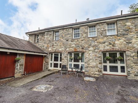 A stone house exterior with windows doors a small patio table and two chairs at Yr Wyddfa in Glasinfryn near Bangor